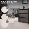 A room setting with a chair and a dresser, showcasing the wood-look flooring. Podgląd zdjęcia produktu