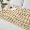 A beige plush blanket is spread out on a bed with white pillows. Produktbild-Vorschau