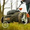 A person is using a lawn mower in a grassy outdoor setting. Produktbild-Vorschau