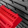 A close-up shot of a red tool organizer with multiple circular holes, placed in front of a stack of black storage boxes. Náhled obrázku produktu