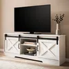 A white TV stand with sliding barn doors, a television on top, and decorative items on the shelves. Náhľad obrázku produktu
