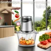 A hand is dropping vegetables into a food chopper, with a kitchen and outdoor scenery in the background. Produktbild-Vorschau