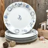 A stack of dinner plates with a nautical theme, set on a sandy surface with wooden background elements. Podgląd zdjęcia produktu
