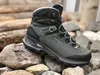 A hiking boot is placed on rocks with logs in the background. Produktbild-Vorschau