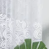 A close-up view of a white lace curtain with a floral pattern. Produktbild-Vorschau