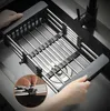 A close-up shot of an adjustable dish drying rack placed inside a kitchen sink, with hands adjusting the rack. Produktbild-Vorschau