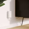 A white Powerline adapter is plugged into a white wall outlet, with several white cables extending from it and running along the baseboard towards a black television. Podgląd zdjęcia produktu