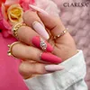 A hand with manicured nails adorned with rhinestones and rings, with pink flowers in the background. Náhled obrázku produktu