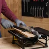 A person wearing gloves is using a table saw to cut a piece of wood in a workshop setting. Anteprima dell’immagine prodotto