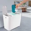 A hand is shown dropping trash into a multi-compartment recycling bin in a modern living room. Náhľad obrázku produktu