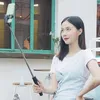 A young woman is taking a selfie with a selfie stick in an outdoor setting. Voir les images du produit