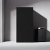 A black metal filing cabinet with sliding doors and a small black nightstand with a white electronic device on top, set against a gray wall with dramatic shadows. Voir les images du produit