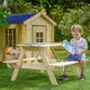 A young child sits at a wooden picnic table in a garden, holding a book. A wooden playhouse is in the background. Anteprima dell’immagine prodotto