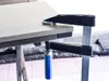 A clamp is attached to the edge of a table. Produktbild-Vorschau