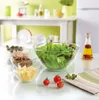 A kitchen counter with ingredients for a salad laid out in bowls, including lettuce, tomatoes, and other toppings, with a bottle of oil and vinegar in the background. Produktbild-Vorschau