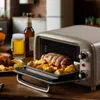 A retro-style toaster oven with a roast and potatoes inside, next to a glass of beer and a bottle of beer. Náhled obrázku produktu