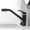 A black kitchen faucet with a silver accent ring is shown on a white countertop next to a sink. Podgląd zdjęcia produktu