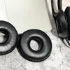 Two black ear pads for headphones are shown on a textured surface next to a laptop and part of a black headphone. Voir les images du produit
