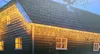 A wooden house with icicle lights on the roof and windows. Produktbild-Vorschau