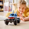 A young girl is playing with a blue LEGO Technic monster truck that resembles a shark. Podgląd zdjęcia produktu