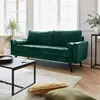 A green velvet sofa is shown in a well-lit living room with a coffee table and floor cushions. Produktbild-Vorschau
