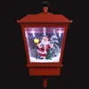 A red Christmas lantern with a Santa Claus figurine inside, a lit lamp post, and a Christmas tree, with artificial snow falling. Produktbild-Vorschau