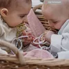 Two babies in a basket, each holding a pacifier and a teething toy. Produktbild-Vorschau