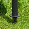 Close-up of a black metal pole with a base plate, partially inserted into green grass. Produktbild-Vorschau