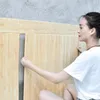 Frau installiert eine hellbraune Holzkern-Schaumstoff-Wandplatte an einer grauen Wand Voir les images du produit