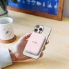 A hand holding a pink power bank attached to a silver smartphone, with a white mug and a plant in the background. Náhled obrázku produktu