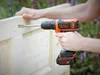 A person is using a Black & Decker cordless drill to make a hole in a wooden door. Podgląd zdjęcia produktu