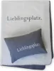 A gray pillow is placed on a white blanket, both featuring the text "Lieblingsplatz." Produktbild-Vorschau