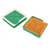 A capsule filling tool with a green base and an orange filling tray, and a separate green and white lid. Voir les images du produit