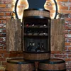 A wooden barrel-shaped wine cabinet with doors open, displaying bottles of wine and liquor on shelves, set against a brick wall with decorative lighting. Náhled obrázku produktu