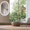 A modern living room with a large window overlooking trees, featuring a mirror, armchair, and coffee table. Anteprima dell’immagine prodotto