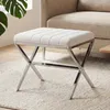 A white upholstered ottoman with a silver metal X-frame base sits on a textured rug next to a beige sofa. Produktbild-Vorschau