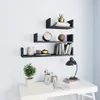 Three black U-shaped shelves mounted on a white wall, decorated with books, a clock, a plant, and decorative items. Below, a white desk with a lamp, a potted plant, and pens in a holder. Anteprima dell’immagine prodotto