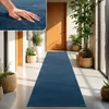 A long blue runner rug is laid out in a hallway with plants and wooden doors. Produktbild-Vorschau