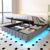 A bed with its storage compartment open, revealing folded clothes and bedding. The bed has LED lighting underneath. Náhľad obrázku produktu