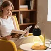 A woman is reading a book while sitting in a chair next to a candle warmer lamp. Náhled obrázku produktu