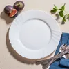A white plate with a decorative rim, set on a light-colored surface, with figs and mint sprigs nearby, and spoons on a blue napkin. Anteprima dell’immagine prodotto