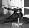 A black and silver furniture lifter is shown in a room with wooden cabinets and a tiled floor. Náhled obrázku produktu