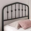A close-up view of a black metal bed frame headboard with decorative elements and pillows on the bed. Podgląd zdjęcia produktu