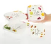 A set of four square plastic food storage containers with lids, each featuring a different food-themed design and text. Produktbild-Vorschau