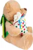 A teddy bear holding a bag with colorful polka dots, wearing a green and yellow strap over its shoulder. Produktbild-Vorschau