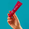 A hand holding a tube of toothpaste against a blue background. Náhled obrázku produktu