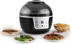 A black and gray air fryer is shown with several plates of food around it, including a quiche, grilled vegetables, and a steak with peppers. Produktbild-Vorschau