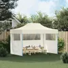 A cream-colored party tent with wooden picnic tables and benches set up on a grassy lawn, with a wooden fence and trees in the background. Náhled obrázku produktu