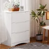 A white dresser with three drawers is placed next to a window with sheer curtains. A potted plant and a chair are also visible. Podgląd zdjęcia produktu