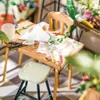 A miniature flower shop scene with a table, chair, and various floral arrangement tools. Náhled obrázku produktu